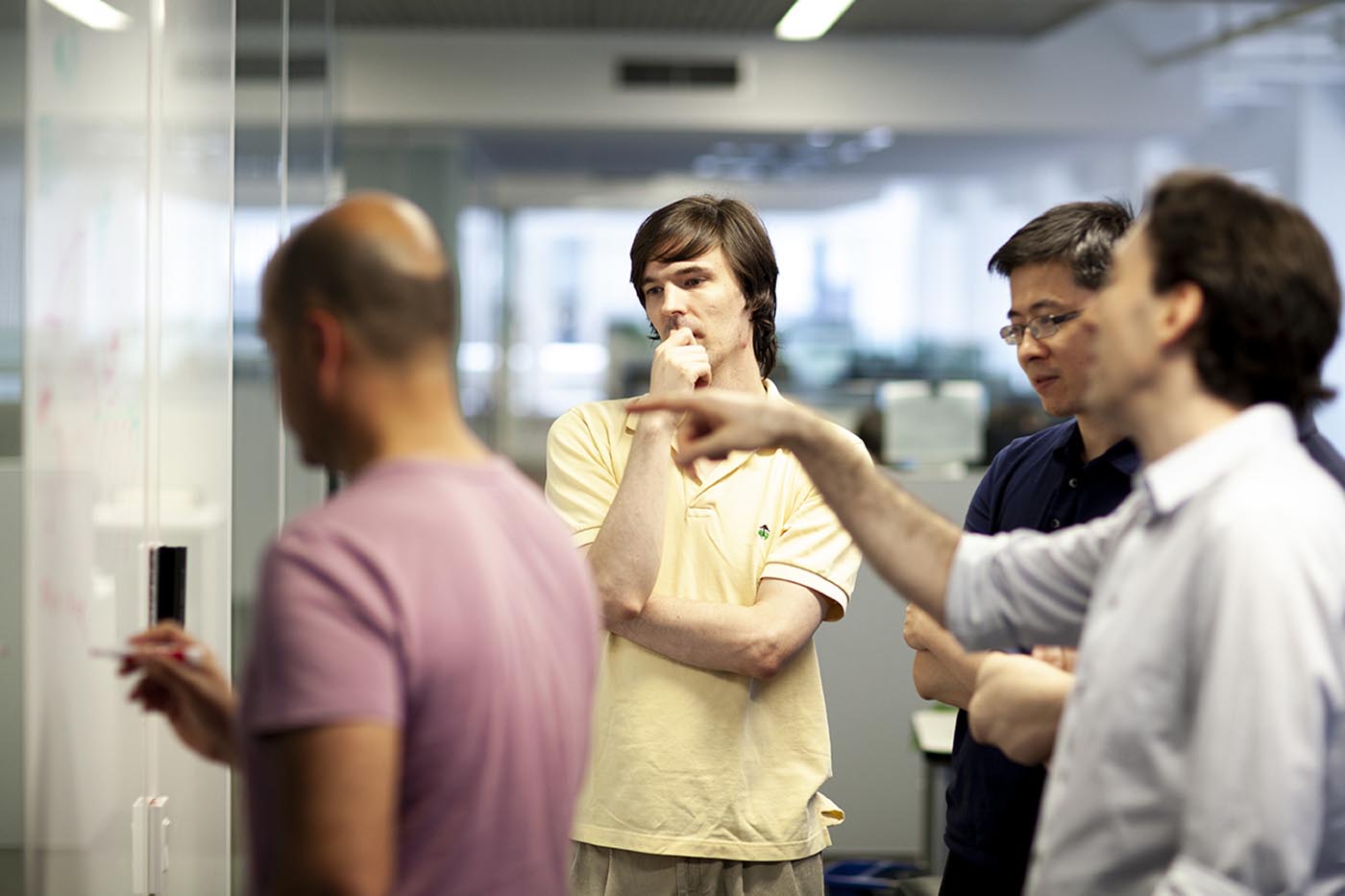 Four investment professionals standing around a whiteboard, thinking and discussing.